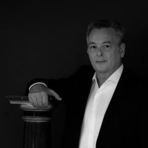 Photo de Philippe Cangémi en costume avec une chemise blanche sans cravate, la main sur une colonne